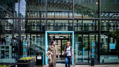 Two students exiting the doors to the Museum of Zoology, glass fronted entrance with suspended whale skelton in the background