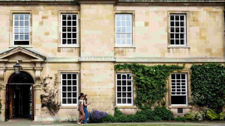 View of Trinity Hall College. Two Students walking past building in front of the lawn.