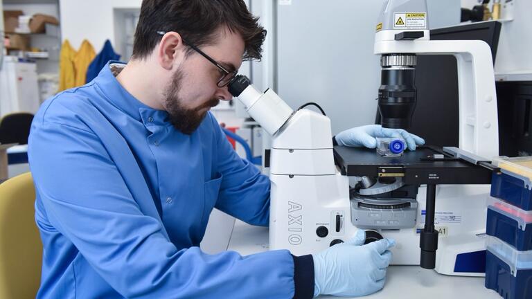Student sitting, looking at sample through a microscope.